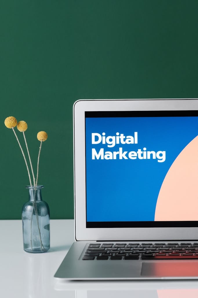 Photo by Mikael Blomkvist A laptop displaying 'Digital Marketing' with a minimalist floral decor in a glass vase.