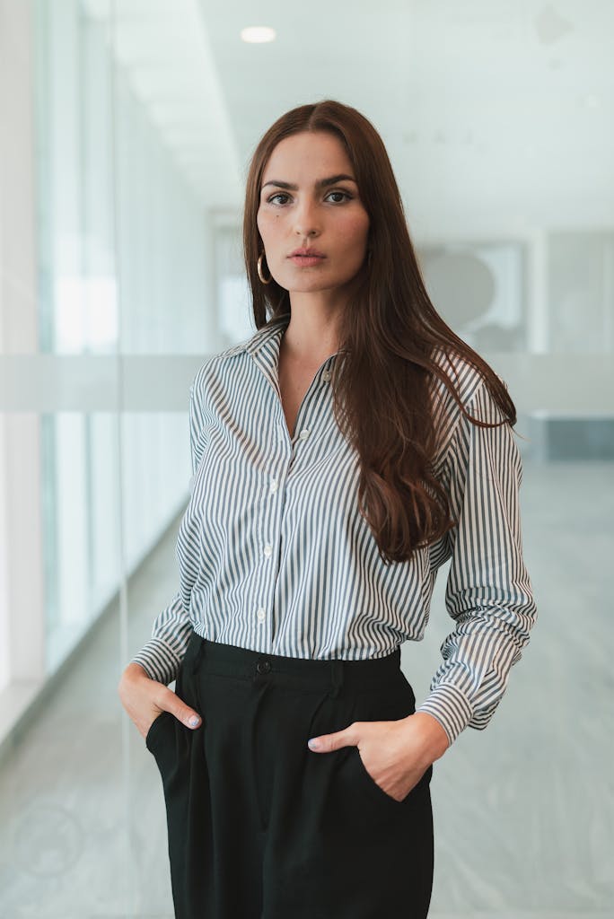 Photo by Los Muertos Crew Businesswoman with brown hair in a striped shirt standing confidently in an office.