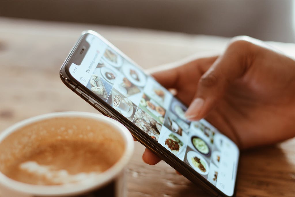 Photo by Kerde Severin Hand browsing social media photos on a smartphone next to a cup of coffee indoors.