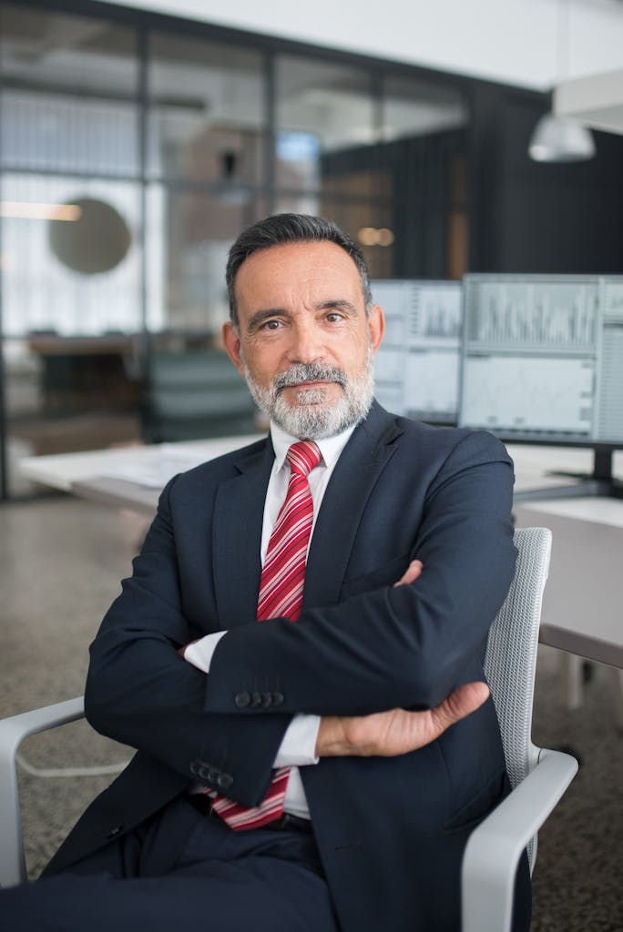 Photo by Kampus Production Professional businessman sitting confidently in a modern office with multiple screens displaying data.