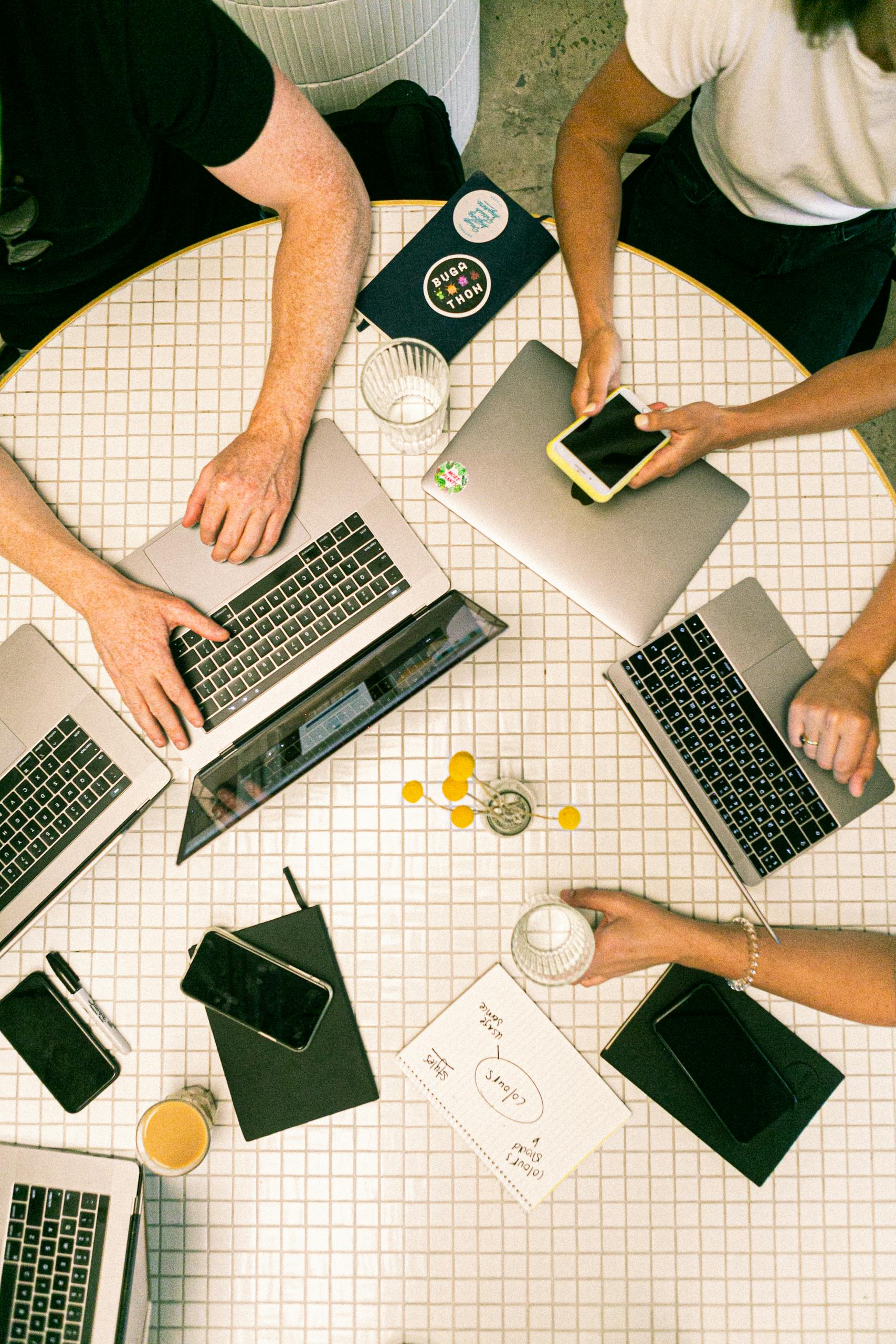 Photo by Canva Studio Top view of a team collaborating with laptops, phones, and notes in a modern office.