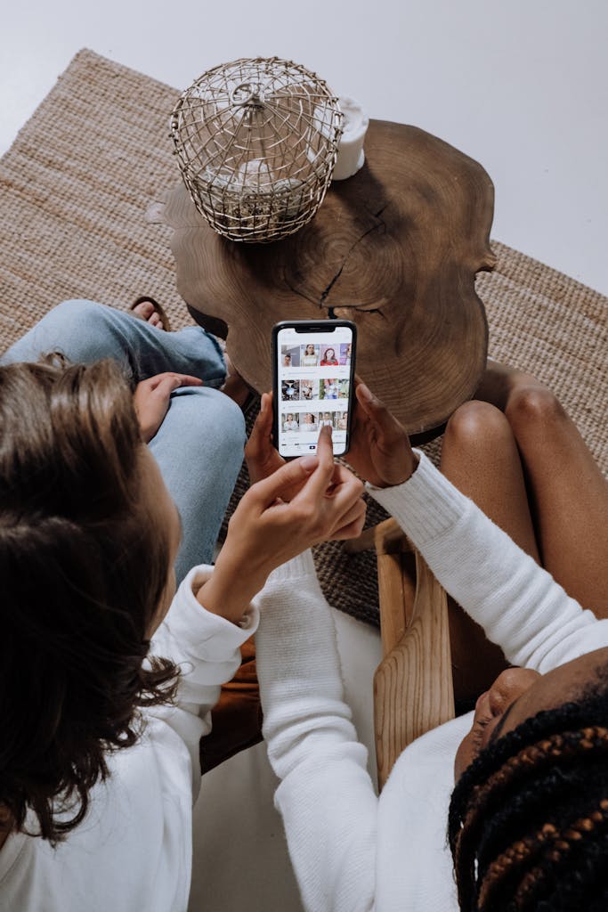 Photo by cottonbro studio Two people looking at social media on a smartphone at a wooden table.