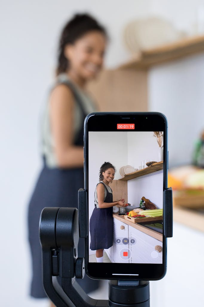 Photo by Ron Lach Woman vlogging her cooking tutorial in a kitchen using smartphone on a tripod.